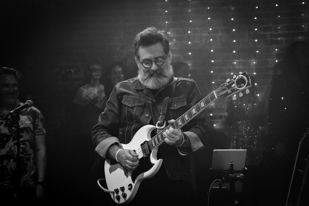 Nick Robinson playing a white Gibson SG on stage, black and white