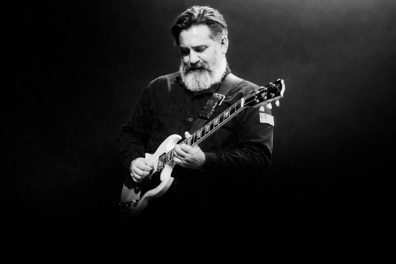 Nick Robinson playing a white Gibson SG on a dark stage